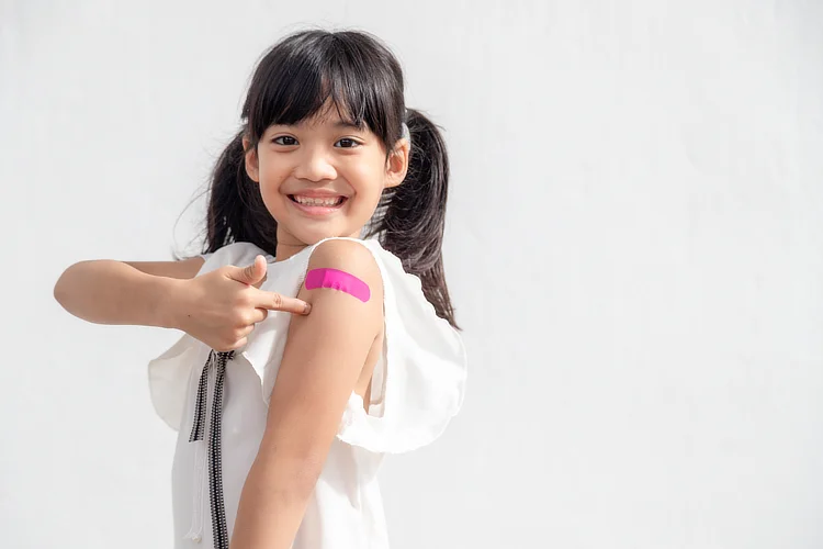 Smiling girl pointing at vaccination plaster on arm, promoting childhood immunisation.