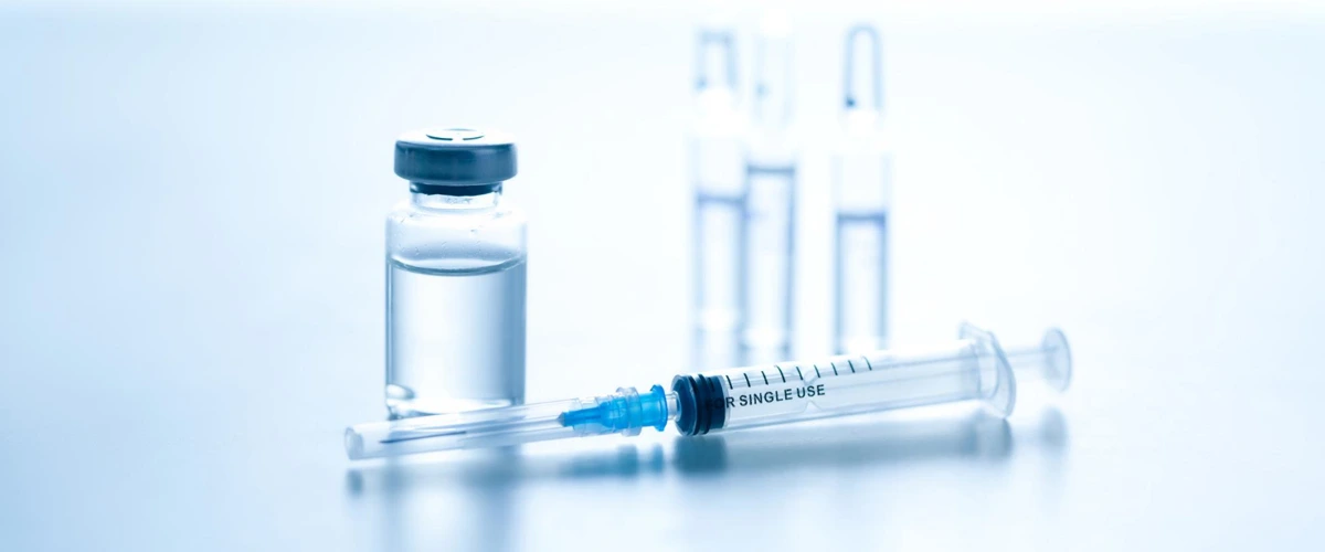 Medical syringe with a bottle storing vaccine next to it.